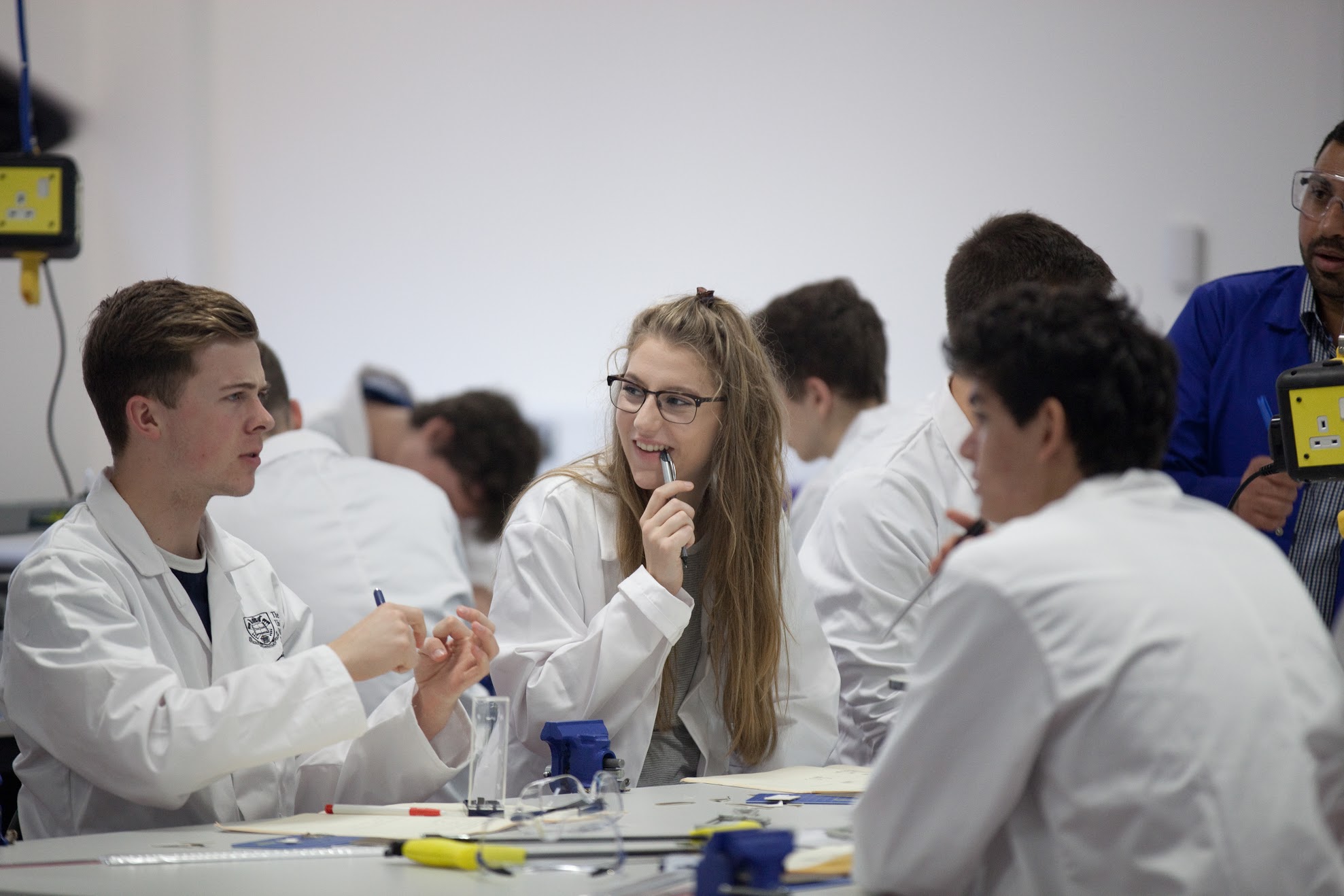 Engineering students in lab coats discuss an experiment