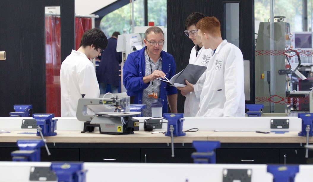 A technician advises engineering students in a workshop environment