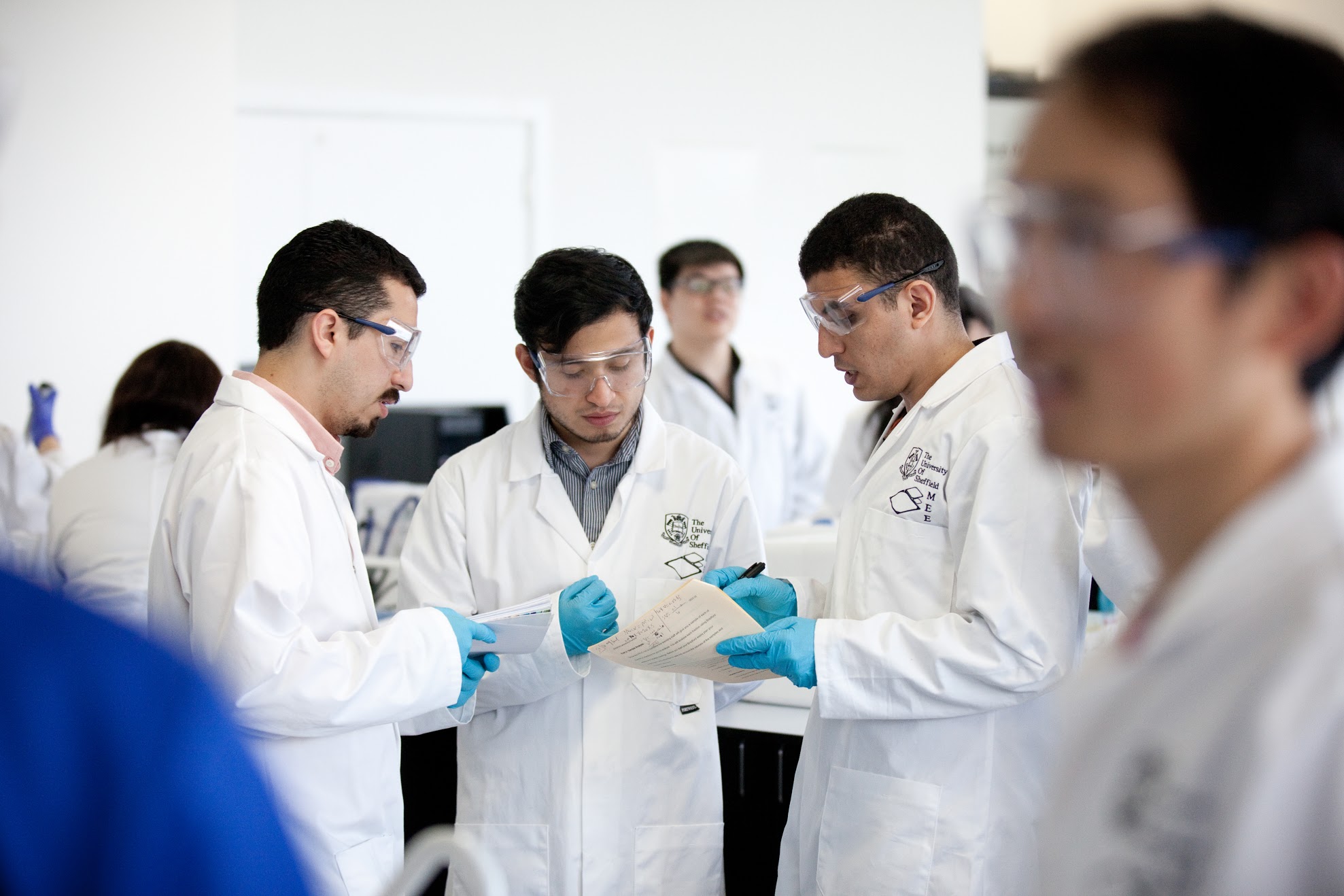 Students in lab coats discuss the findings in a report